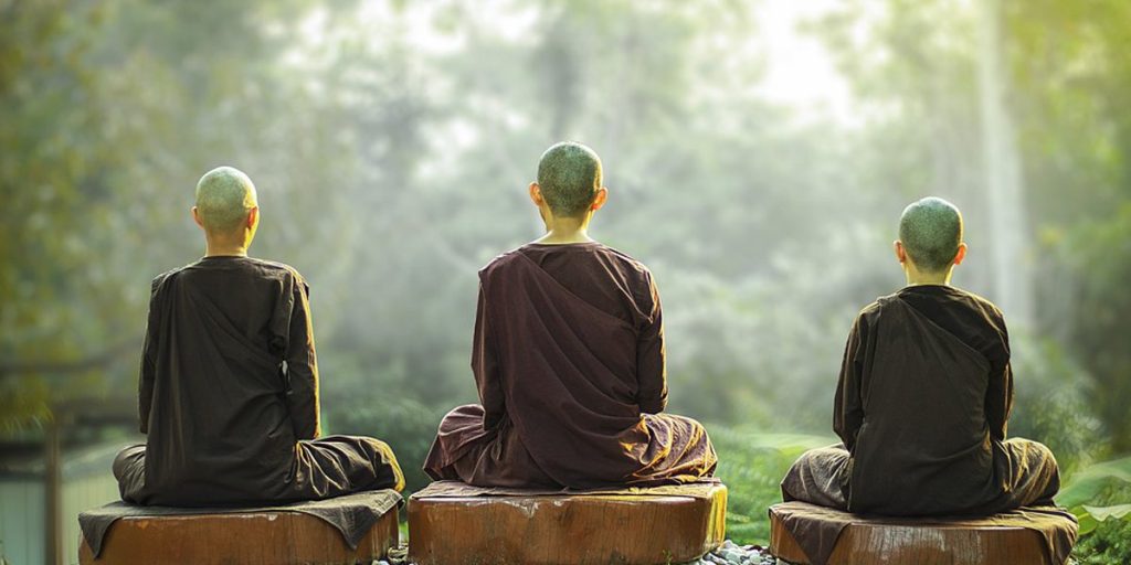 Trois moines bouddhistes en pleine méditation (Buddhist monks meditating) au cœur d’une forêt luxuriante. Vue de dos des moines en robes traditionnelles during a mindfulness session in nature pour le calme et la sérénité.