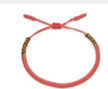 Bracelet tressé tibétain rouge ajustable avec nœud coulissant et détails dorés et noirs. Adjustable red Tibetan braided bracelet with sliding knot and small gold and black accents.