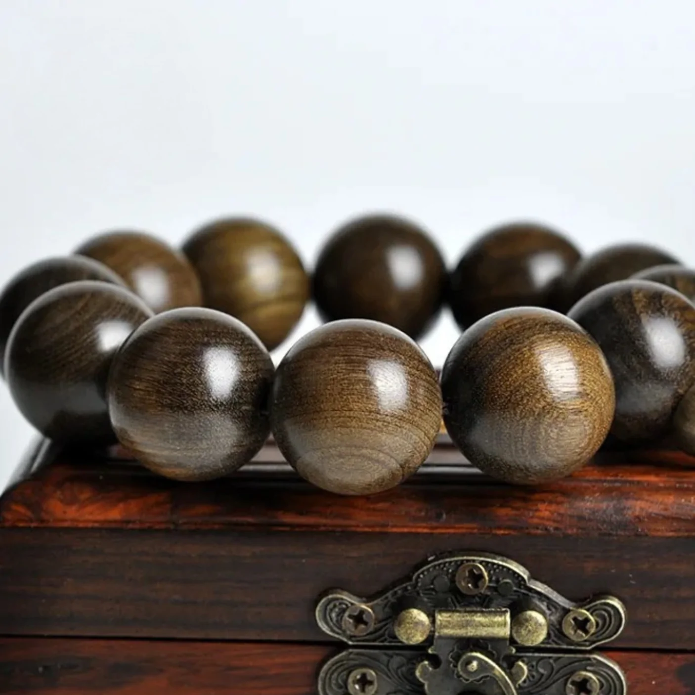 Bracelet mala en perles de bois brun foncé poli, gros plan sur boîtier en bois avec fermoir métal. Dark brown polished wood mala bracelet beads close-up on a wooden box with metal clasp.
