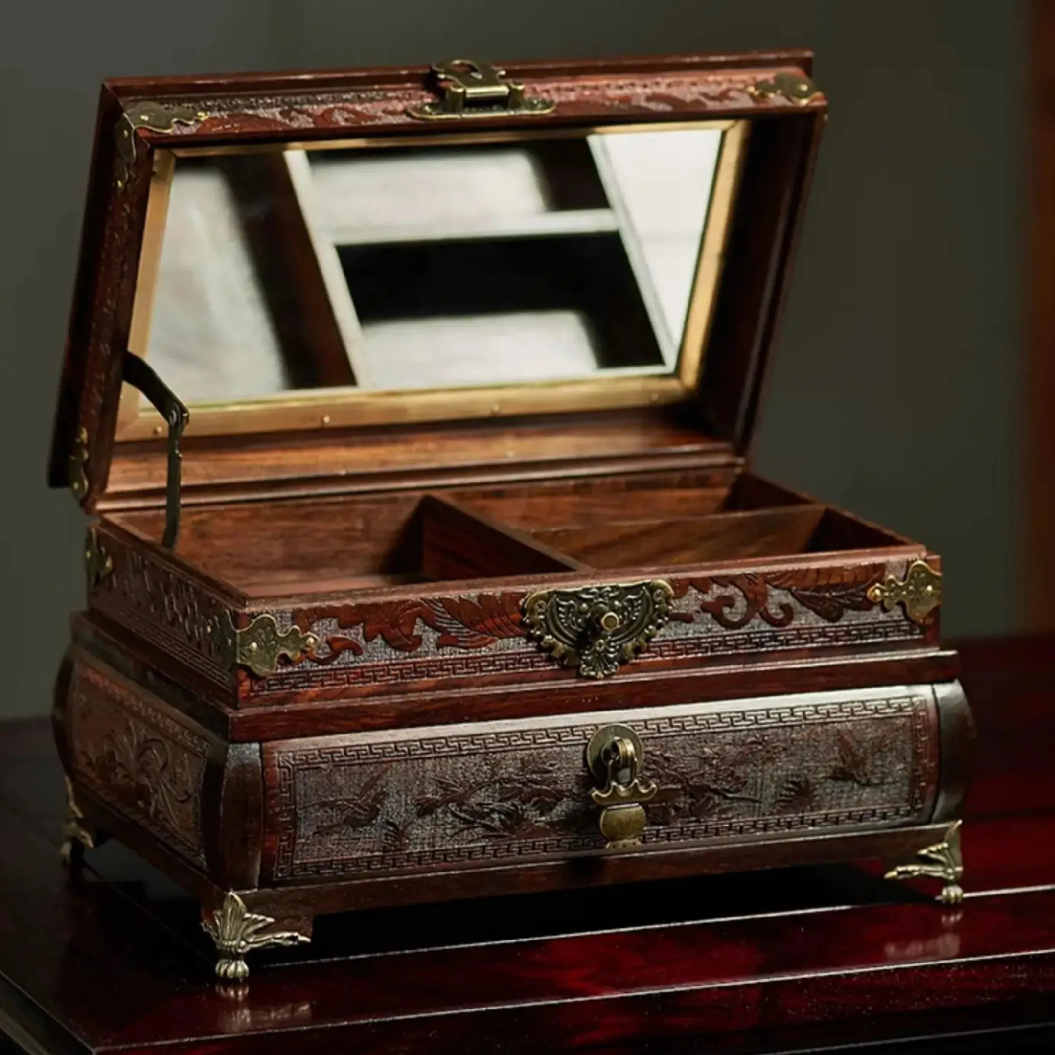 Boîte à bijoux en bois de rose sculpté avec miroir intégré, compartiments et tiroir, finitions métal couleur laiton. Carved rosewood jewelry box with mirror, compartments and drawer, brass-tone metal details.