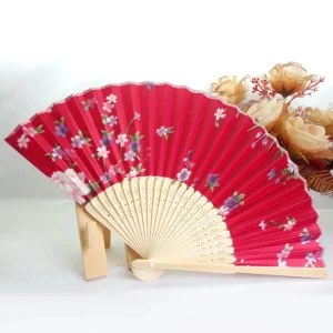 Chinese silk folding fan, deep crimson-rose background with white plum blossoms, pink flowers and violet accents, bamboo ribs