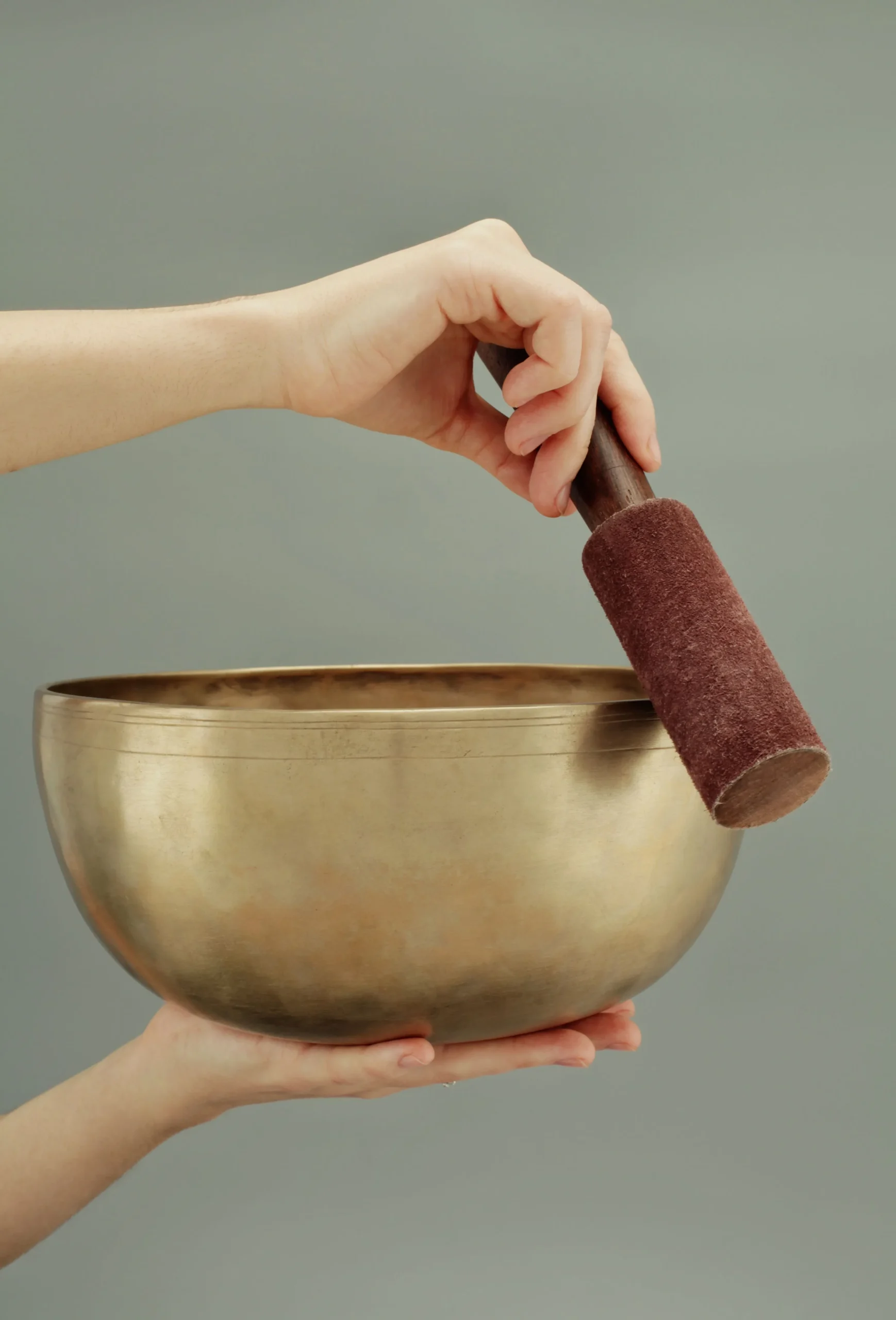 Hands holding and playing a Tibetan copper singing bowl — palm placement, mallet technique