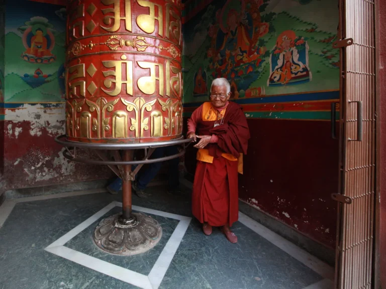 Moine bouddhiste en robe safran tenant un moulin a prieres a main, Tibet