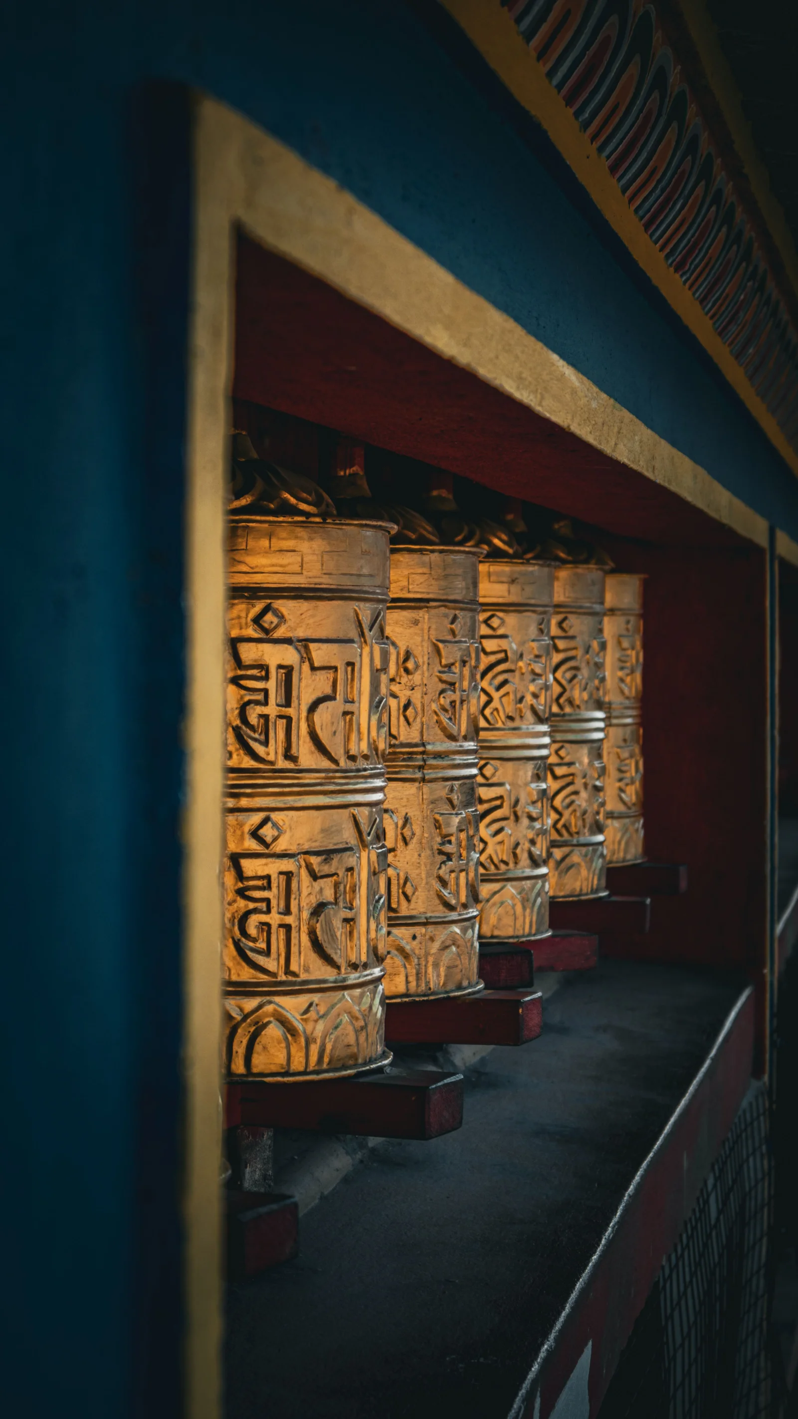 Row of gilded Tibetan prayer wheels in hammered metal, Tibet