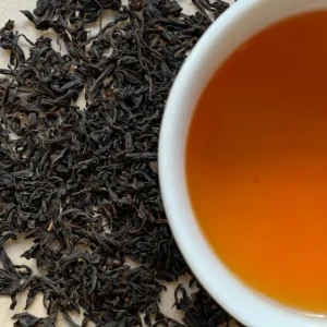 Feuilles de the noir fume Lapsang Souchong et tasse de liqueur ambree vue de dessus