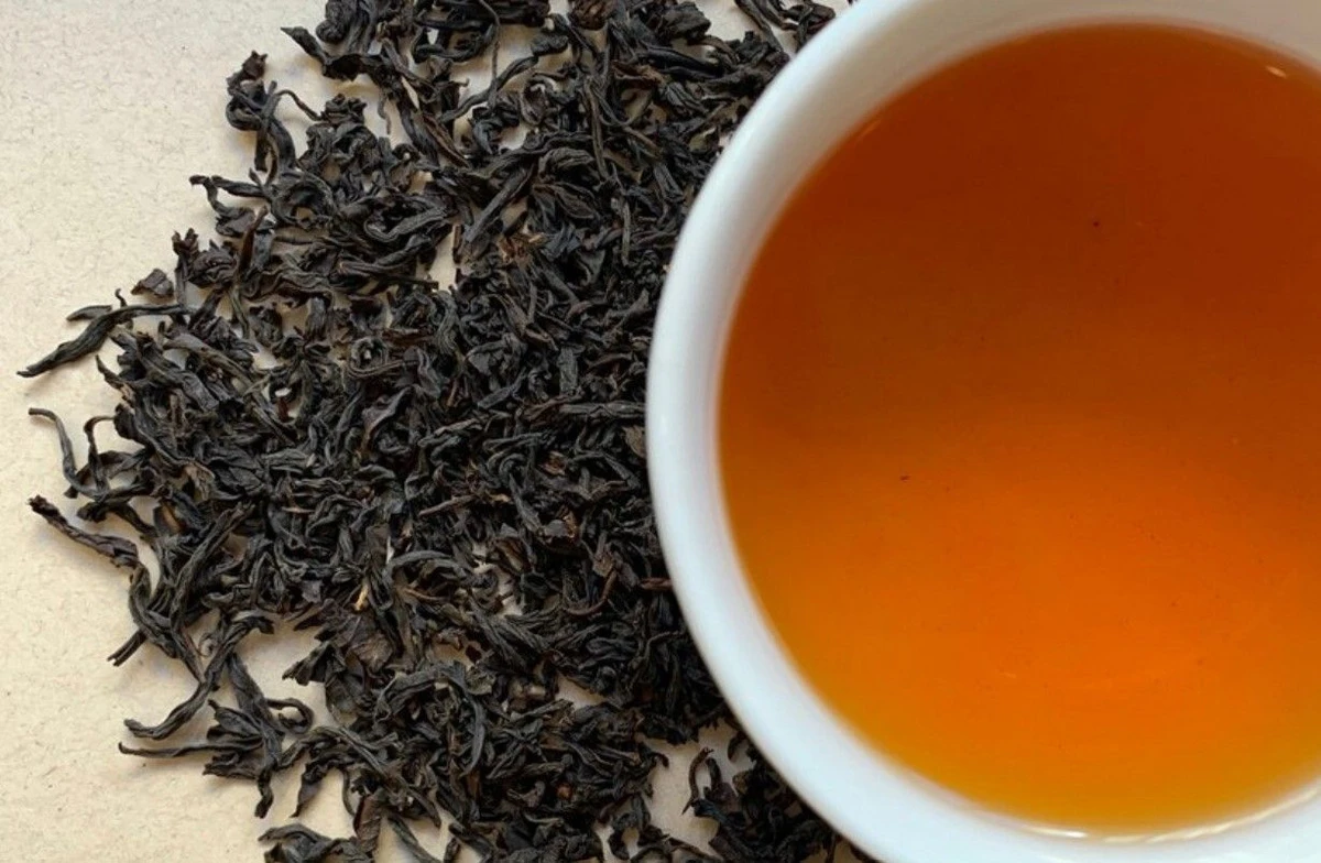 Feuilles de the noir fume Lapsang Souchong et tasse de liqueur ambree vue de dessus